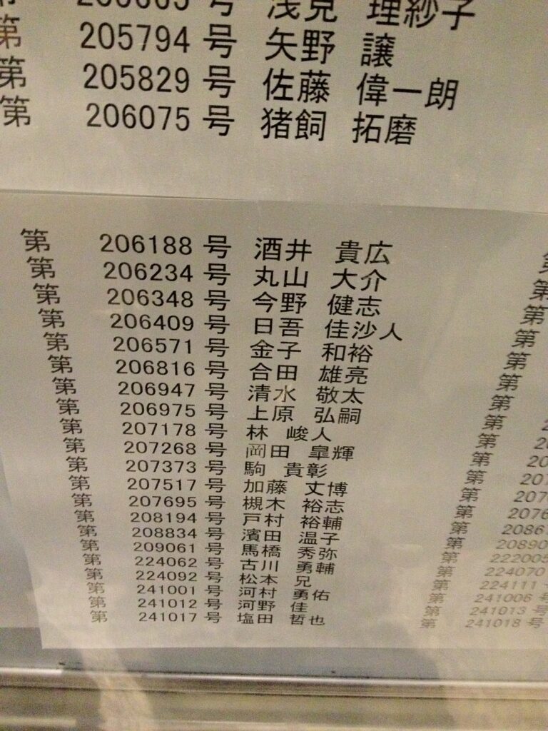 平成24年公認会計士試験の合格発表掲示板。金融庁に張り出された丸山大介の名前と受験番号（逆転の帝王学 第2章）